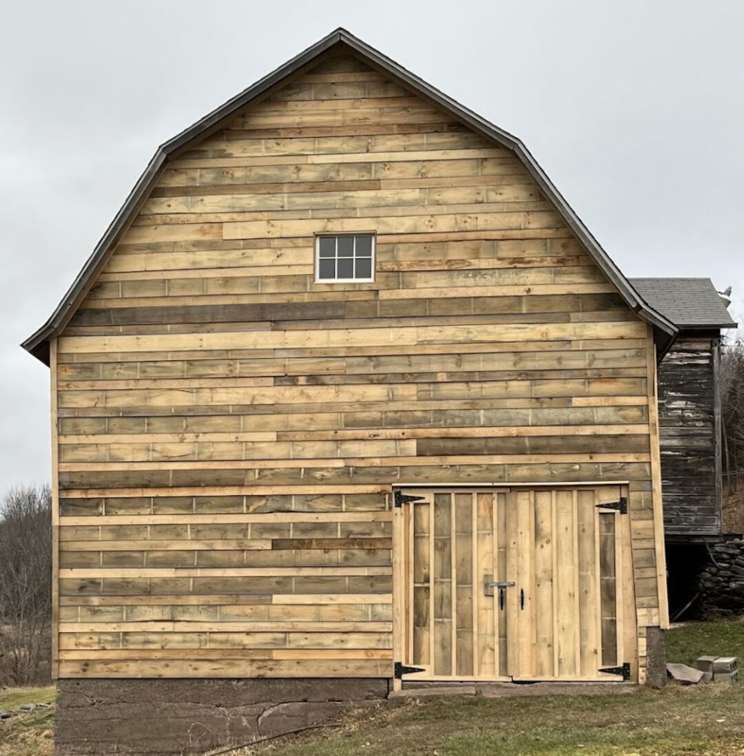 A large wooden barn with a symmetric design, featuring a small square window near the top and a prominent set of double doors.